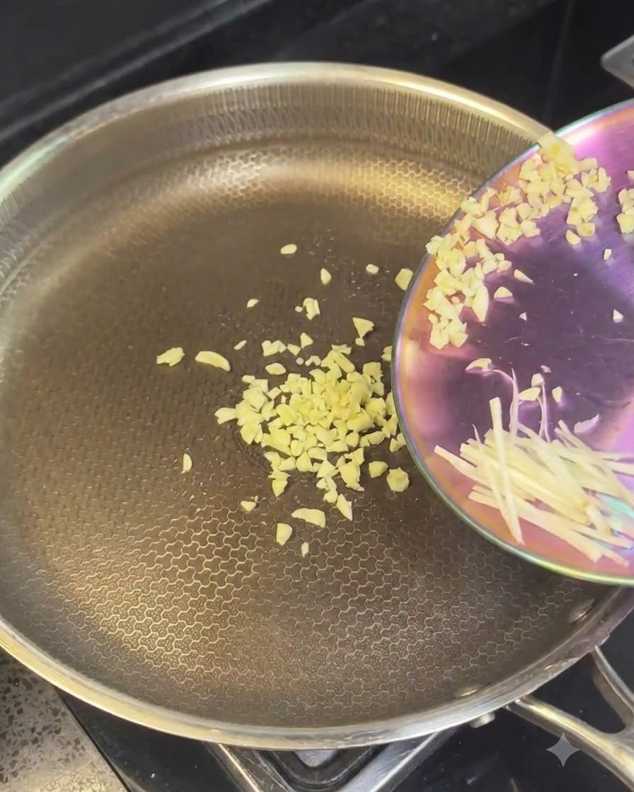 Minced garlic and sliced onions being poured into a hot stainless steel pan.