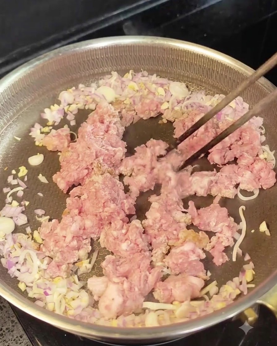 Raw minced meat placed in the center of a pan surrounded by sautéed onions and garlic.
