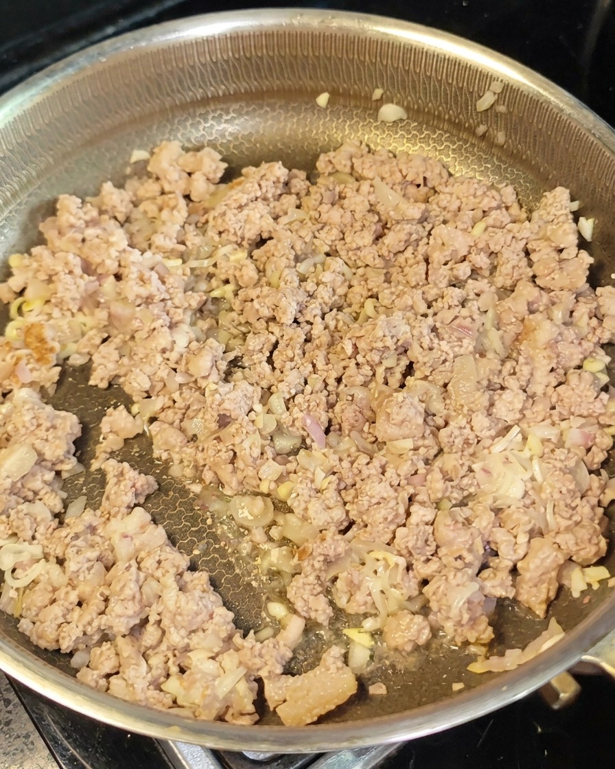 Browned minced meat and aromatics spread out in a pan with red miso paste being incorporated.