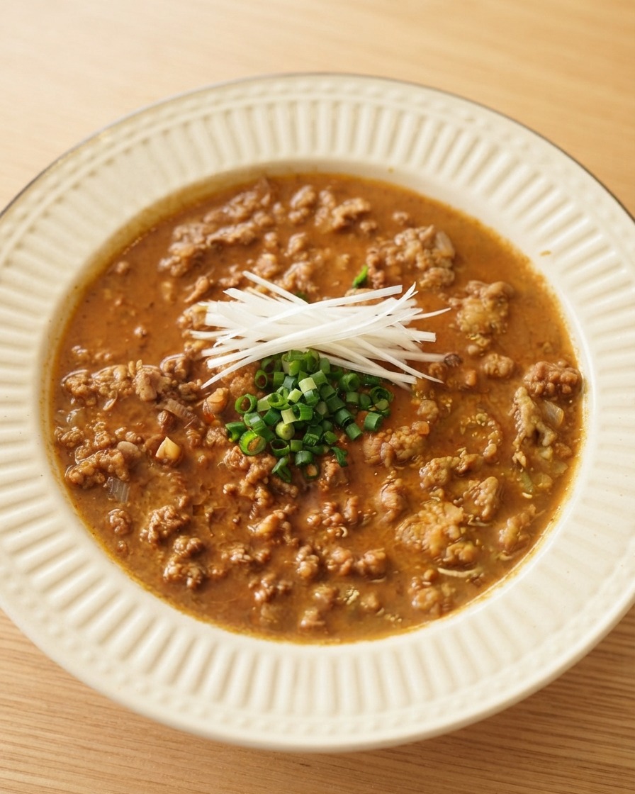 Thin white scallion strips and chopped green onions arranged neatly on top of rich meat sauce in a white serving bowl.
