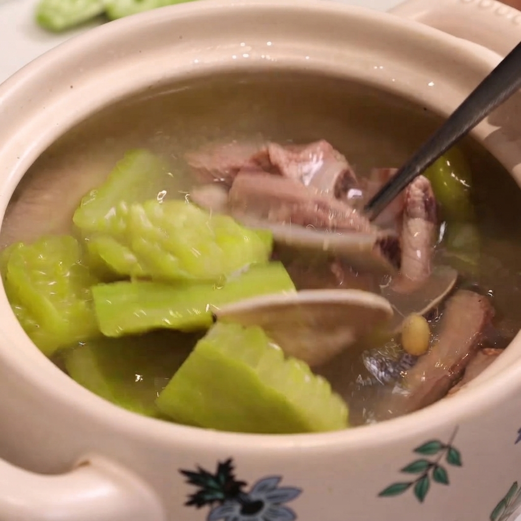 A metal spoon scoops out cooked pork ribs, clams, and bitter melon from a pot of soup.