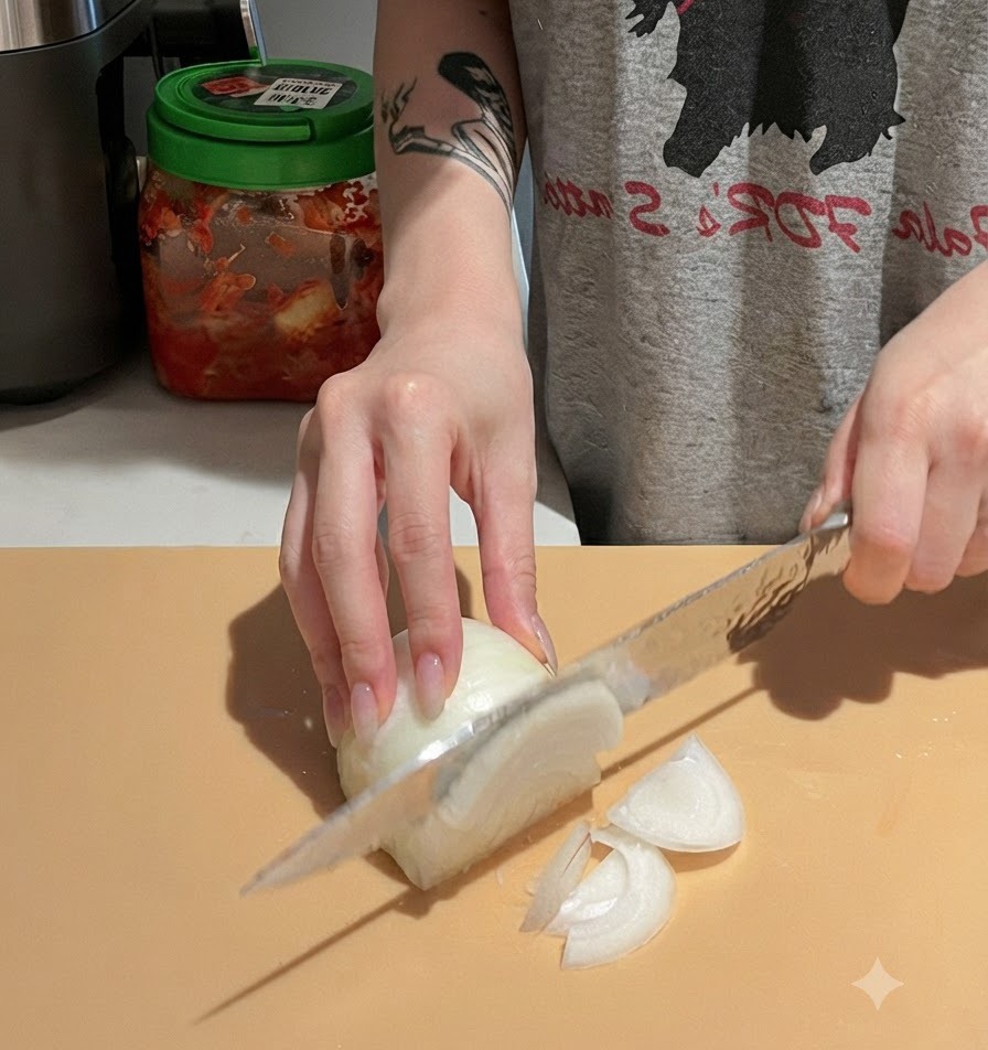 Hands carefully slicing a white onion on a cutting board using a chefs knife.