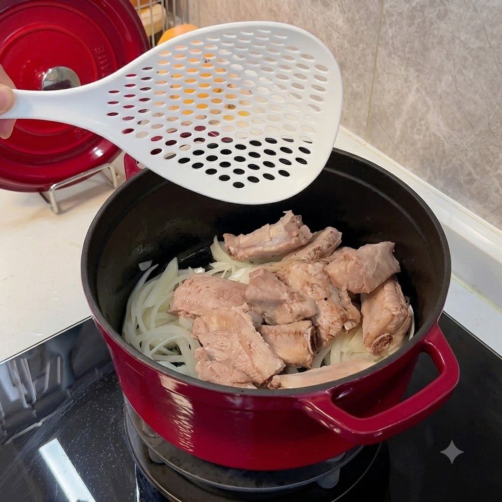 Placing blanched pork ribs into a red pot over a bed of softened onions using a white skimmer.