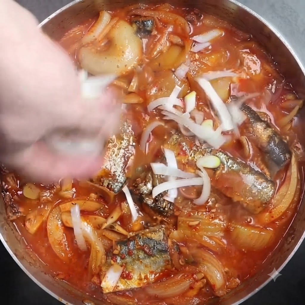 Chopped white scallions being sprinkled over a simmering pot of braised fish.