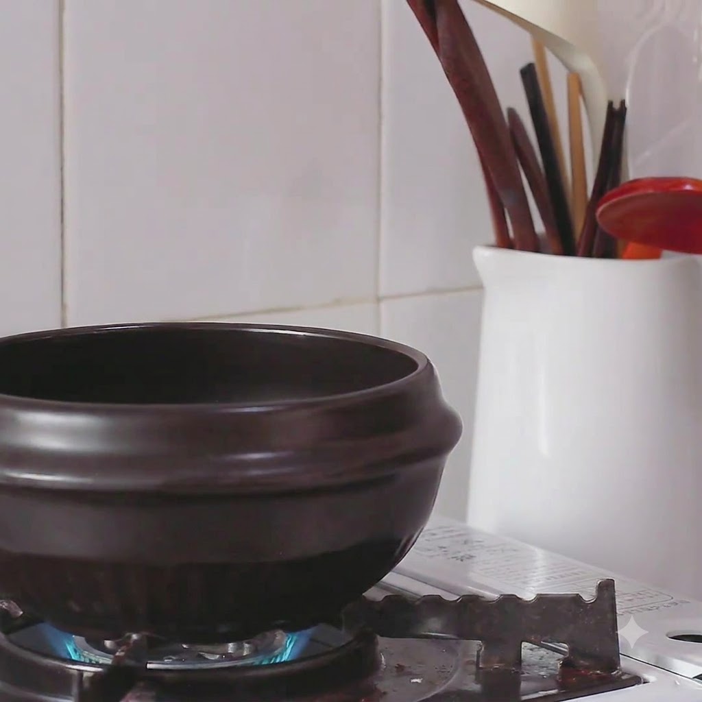 Oil being poured from a tuna can into a warm black earthenware pot on a burner.