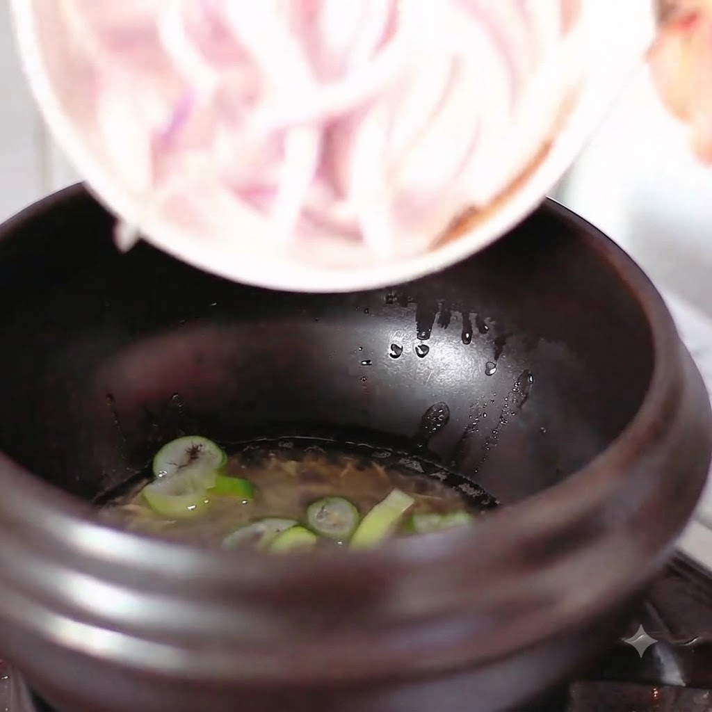 Sliced red onions falling from a small white bowl into a pot with oil and chopped scallions.