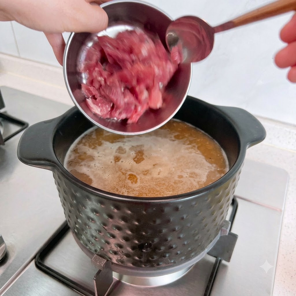 Raw pork pieces being poured from a metal bowl into a pot of boiling soup.