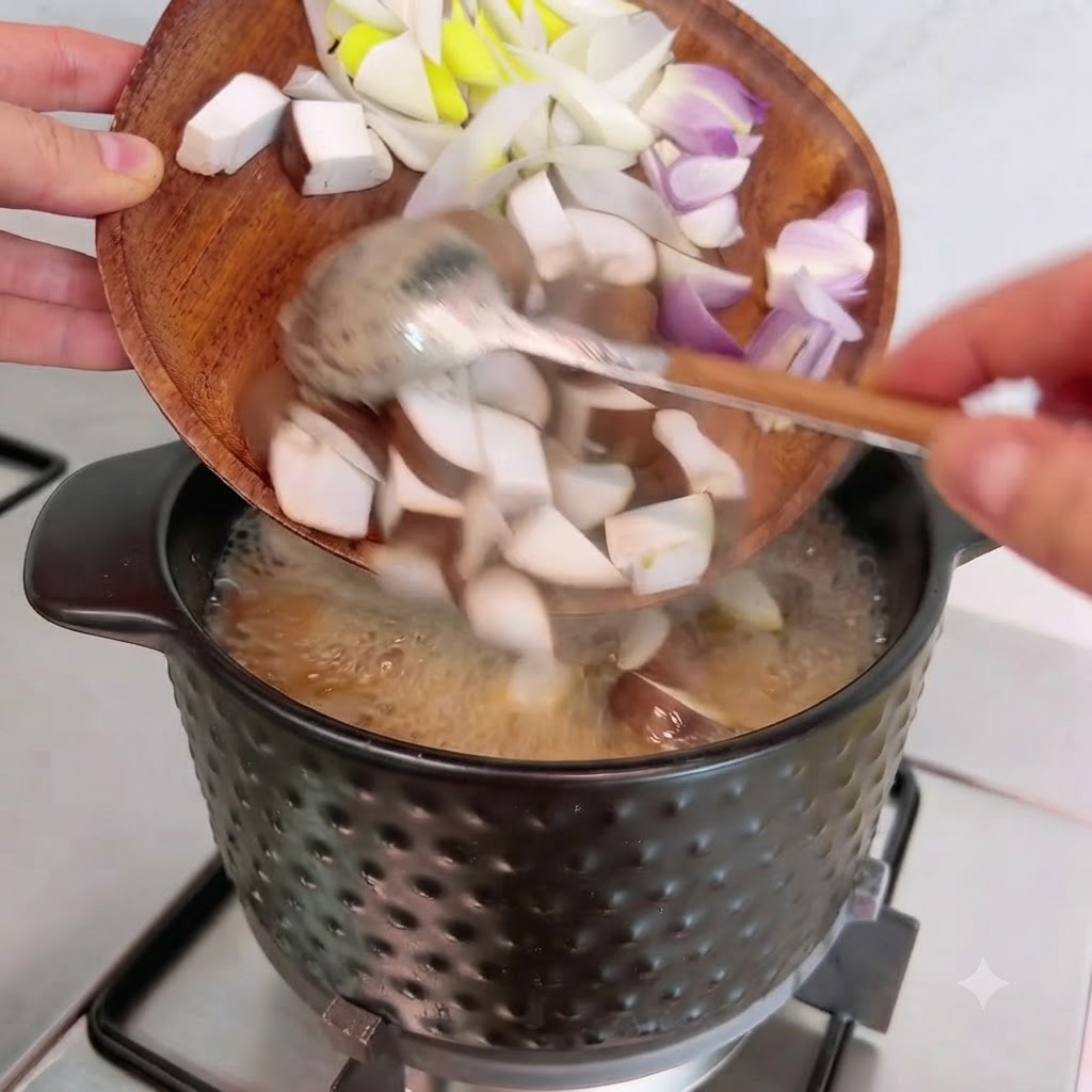 Diced shiitake mushrooms, onions, and scallions being tipped from a wooden plate into the pot.
