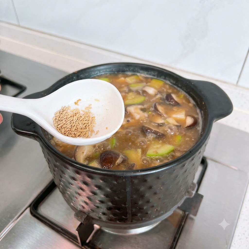 A white spoon holding beef bouillon powder positioned over a bubbling pot of Doenjang Jjigae.
