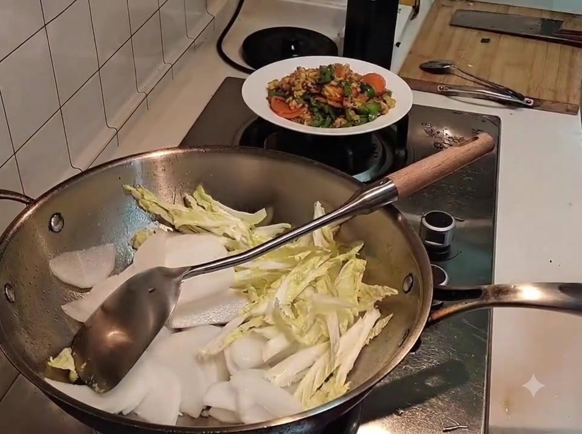 Sliced white radish resting on top of slightly wilted napa cabbage inside a metal wok, with a spatula nearby.