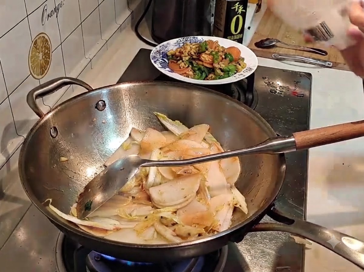 Salt being sprinkled from a packet into a wok containing sliced vegetables.