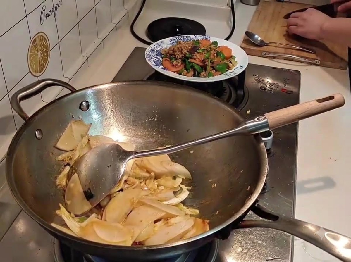 Water being poured from a black kettle into a wok filled with sliced radish and cabbage.