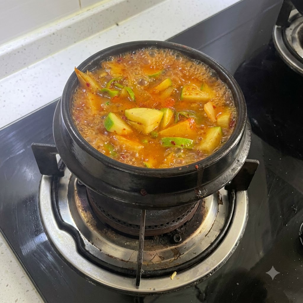 A bubbling pot of spicy orange-red stew simmering on a gas stove burner.