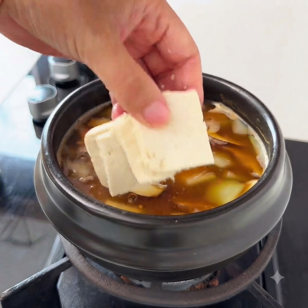 Pieces of tofu being added to the soup containing zucchini slices and enoki mushrooms.