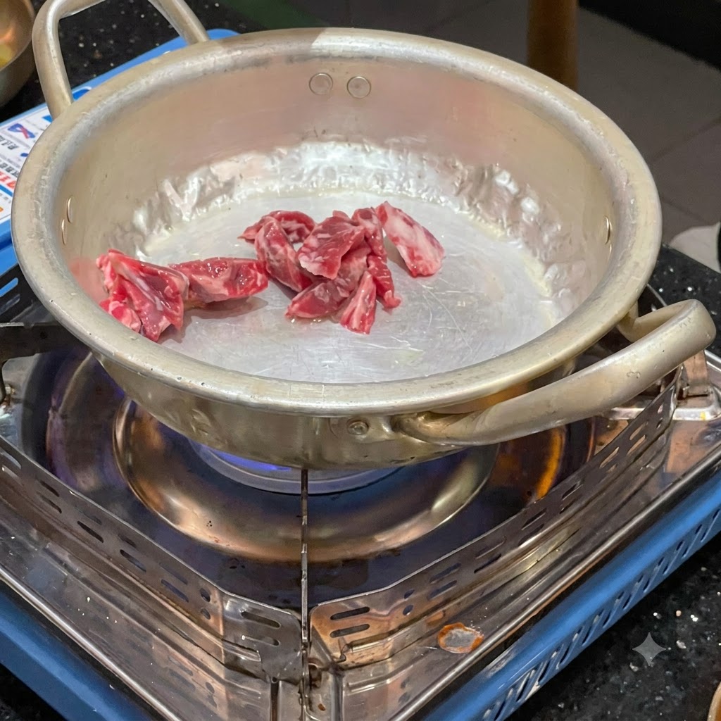 Raw beef pieces being stir-fried in a small metal pot over a lit portable gas burner.
