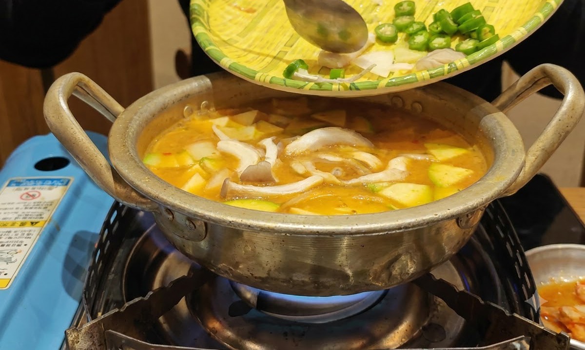 Prepped vegetables being slid from a woven tray into the boiling pot of stew.