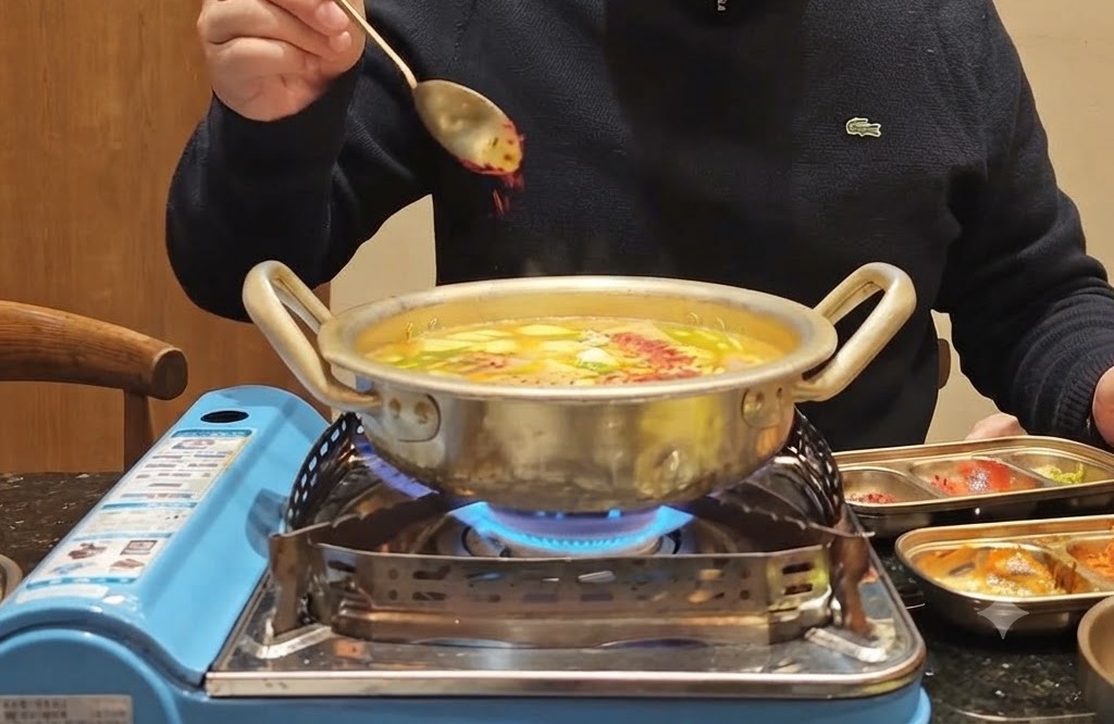 A spoonful of red chili powder being sprinkled over a bubbling pot filled with vegetables and broth.