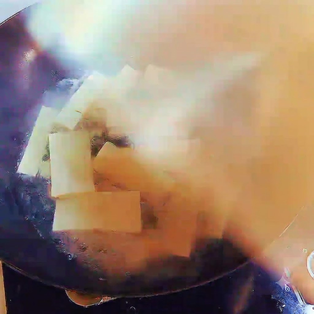 A wok filled with boiling soup and tofu strips, covered securely with a lid.