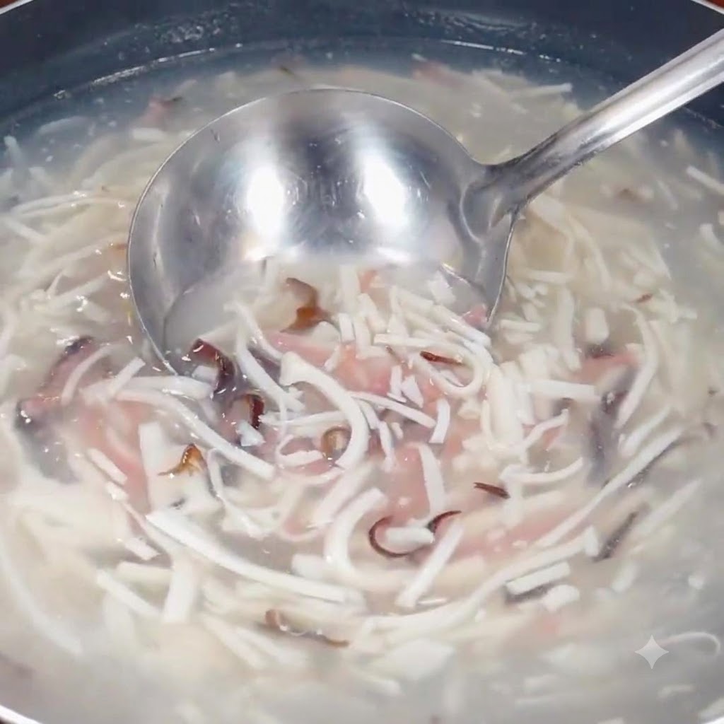 A ladle scooping through the simmering soup mixture containing shredded ingredients in a pot.