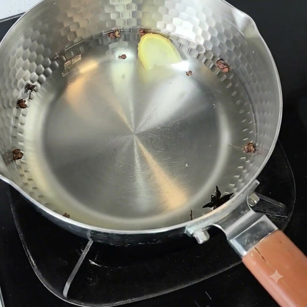 A metal pot filled with cold water, Sichuan peppercorns, star anise, and a ginger slice sitting on a burner.