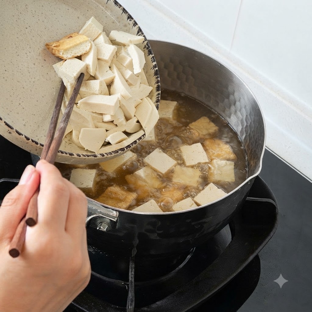 Chopsticks guiding sliced tofu and wood ear mushrooms from a plate into a pot of boiling soup.