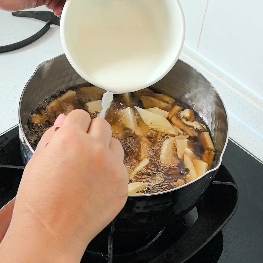 Water starch being poured from a white bowl into a bubbling pot of soup.