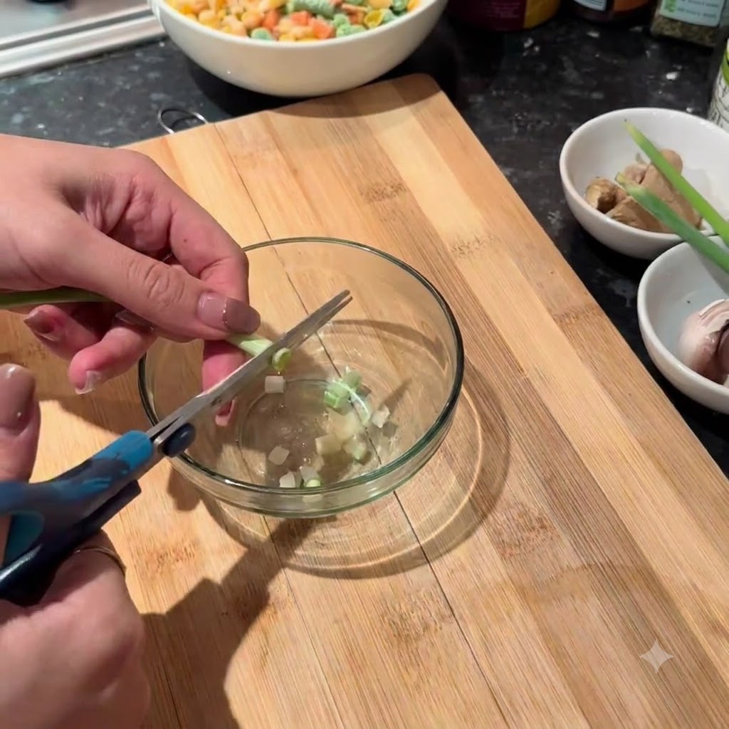 Green scallion stalks being cut into small pieces with scissors into a glass bowl.