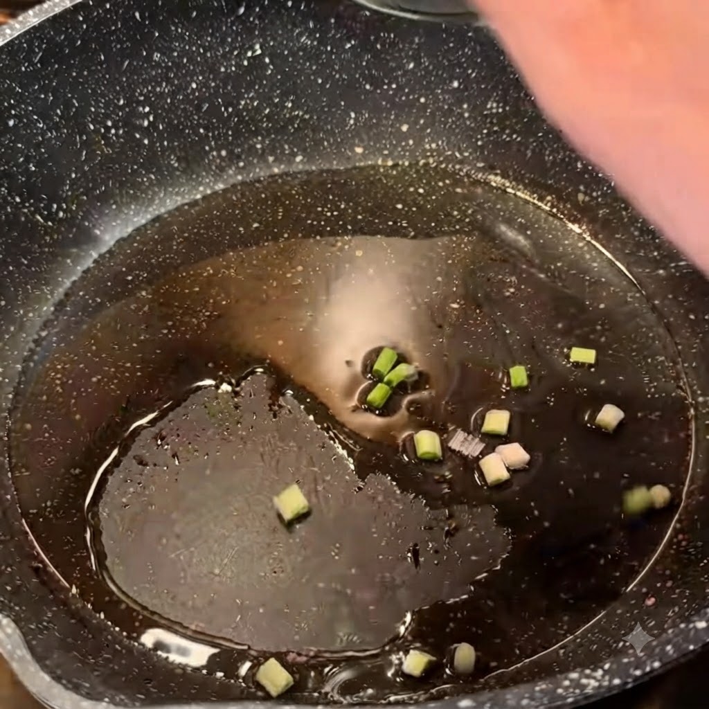 Chopped green onions sizzling in hot oil inside a dark frying pan.