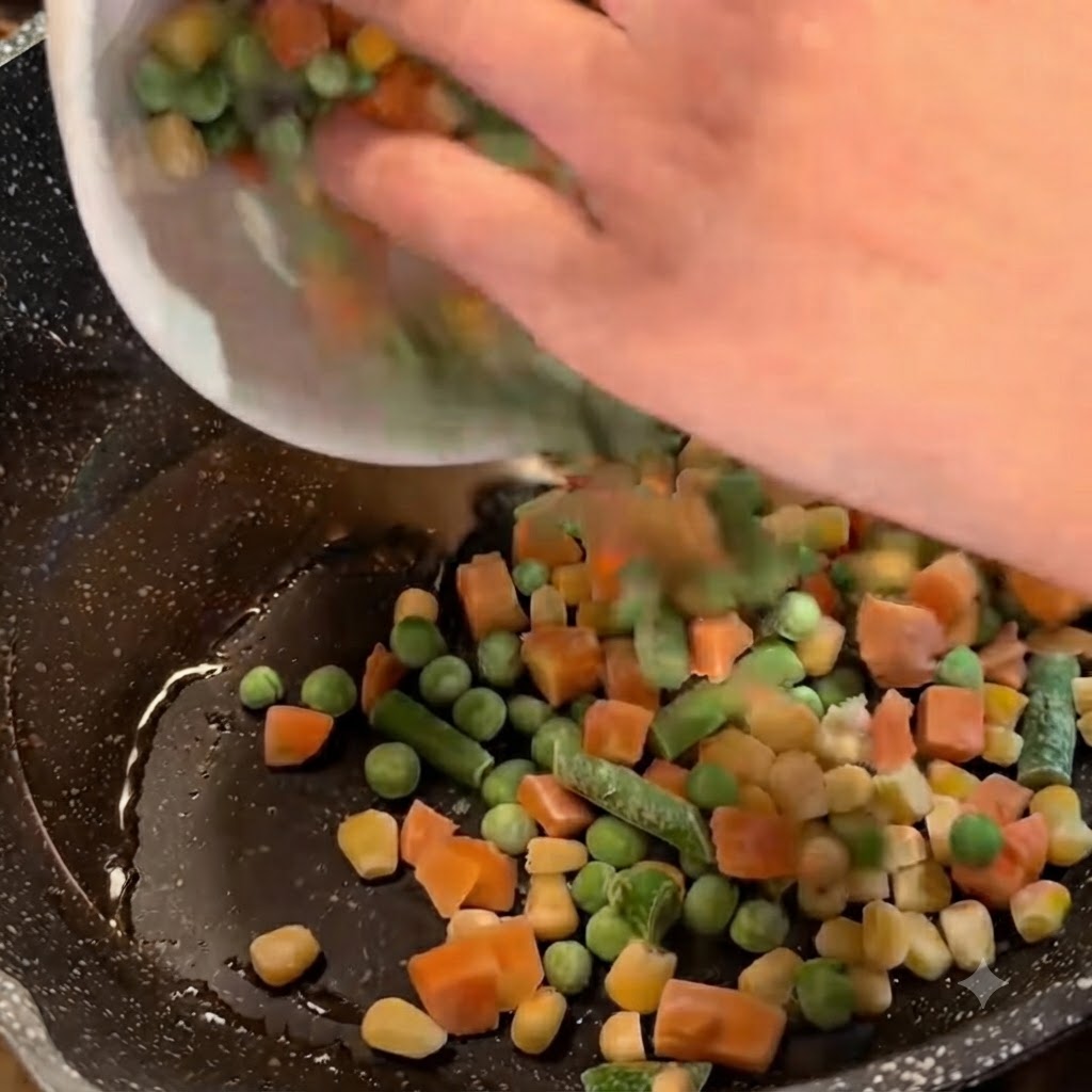 Frozen mixed vegetables being poured from a white bowl into a frying pan with oil and scallions.