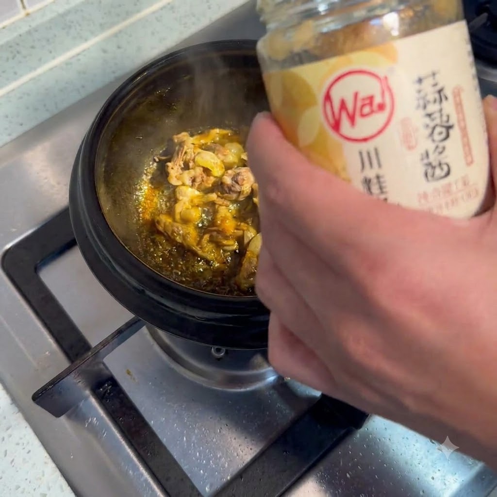 A spoonful of garlic paste being scooped and added into a sizzling pot of meat.