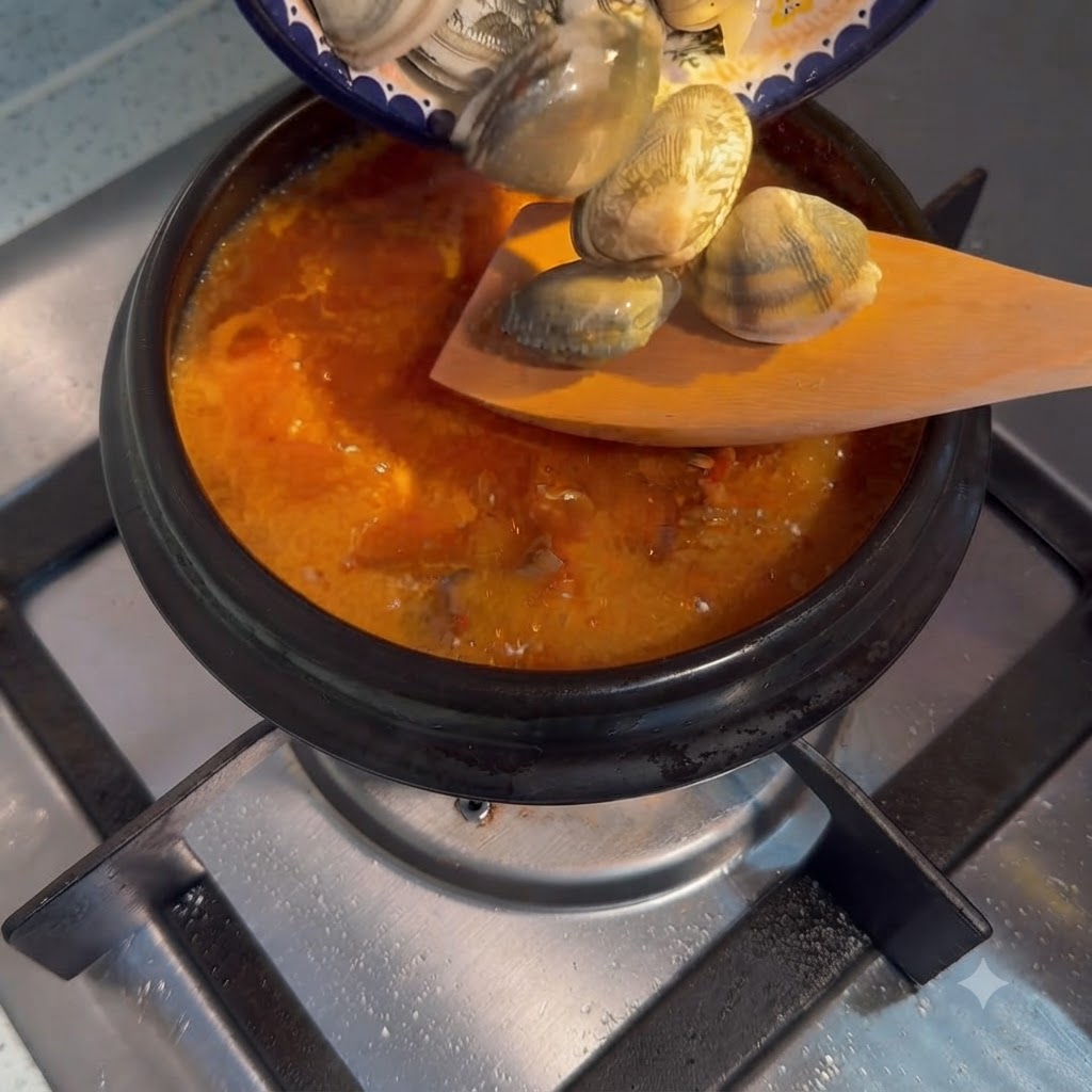 Fresh clams being poured from a small plate into a bubbling pot of Korean soft tofu stew.