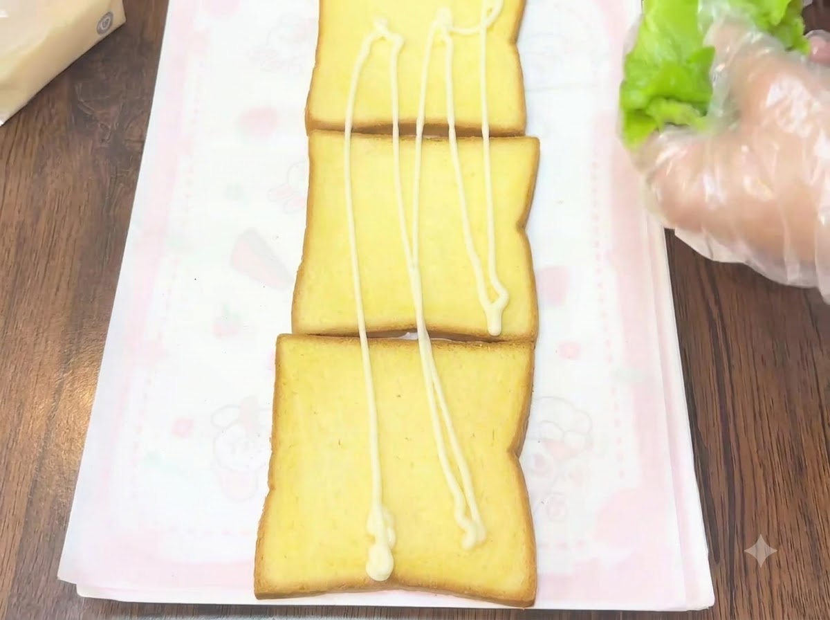 A gloved hand placing fresh green lettuce leaves onto a slice of toast with dressing on it.