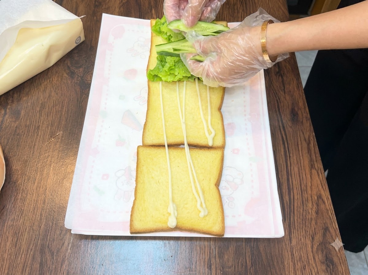Hands arranging fresh green cucumber slices over a bed of lettuce on a piece of toast.