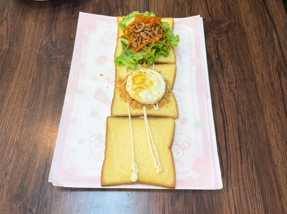 A freshly fried egg sitting on top of a layer of savory meat floss and seaweed crumbs on a slice of toast.