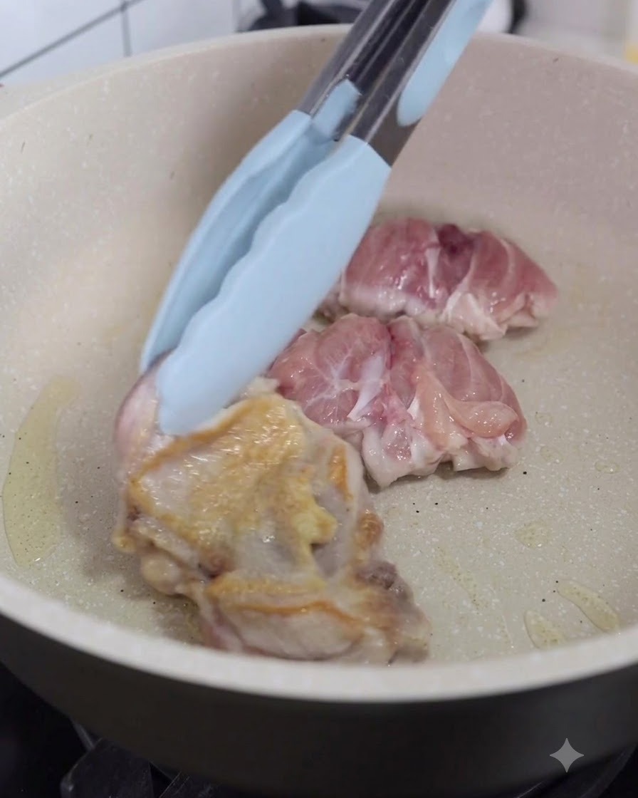 Chicken pieces being turned over in the pan using kitchen tongs.