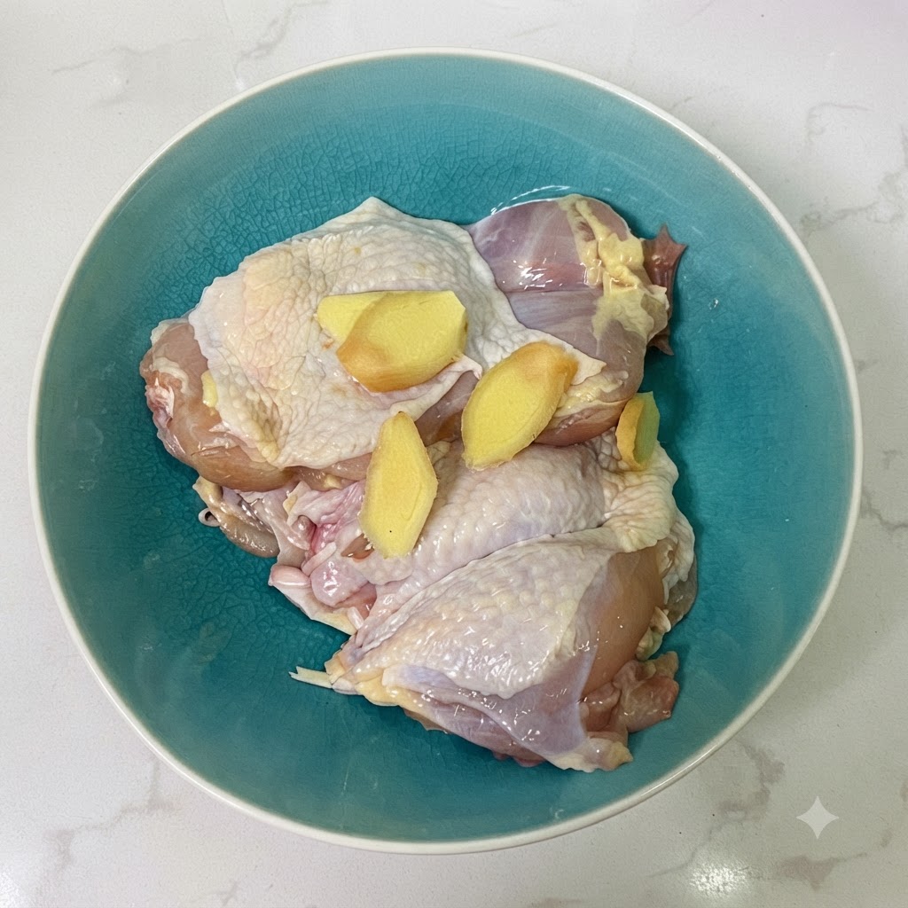 Chicken thighs and ginger slices inside a blue ceramic bowl with soy sauce.