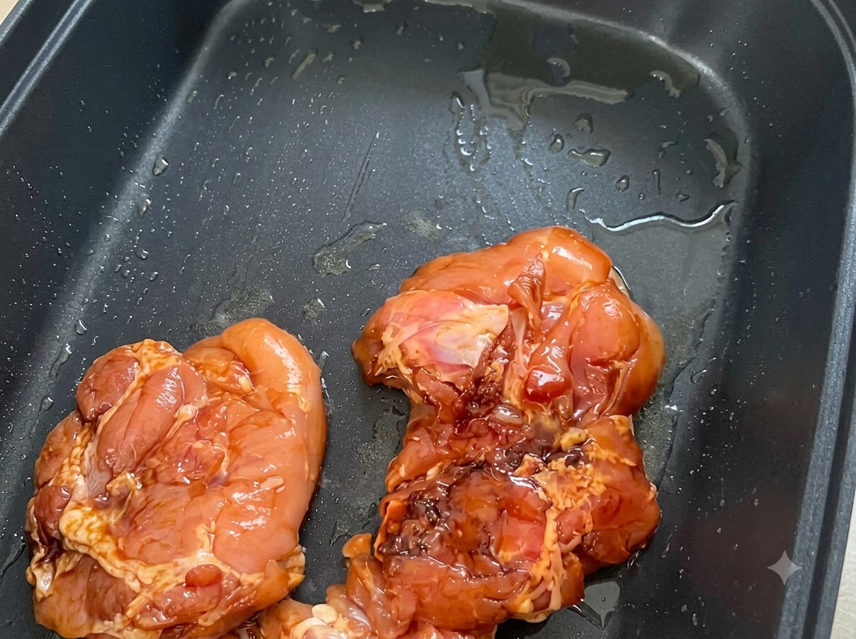 Marinated chicken pieces arranged skin side down in a greased black non-stick pan.