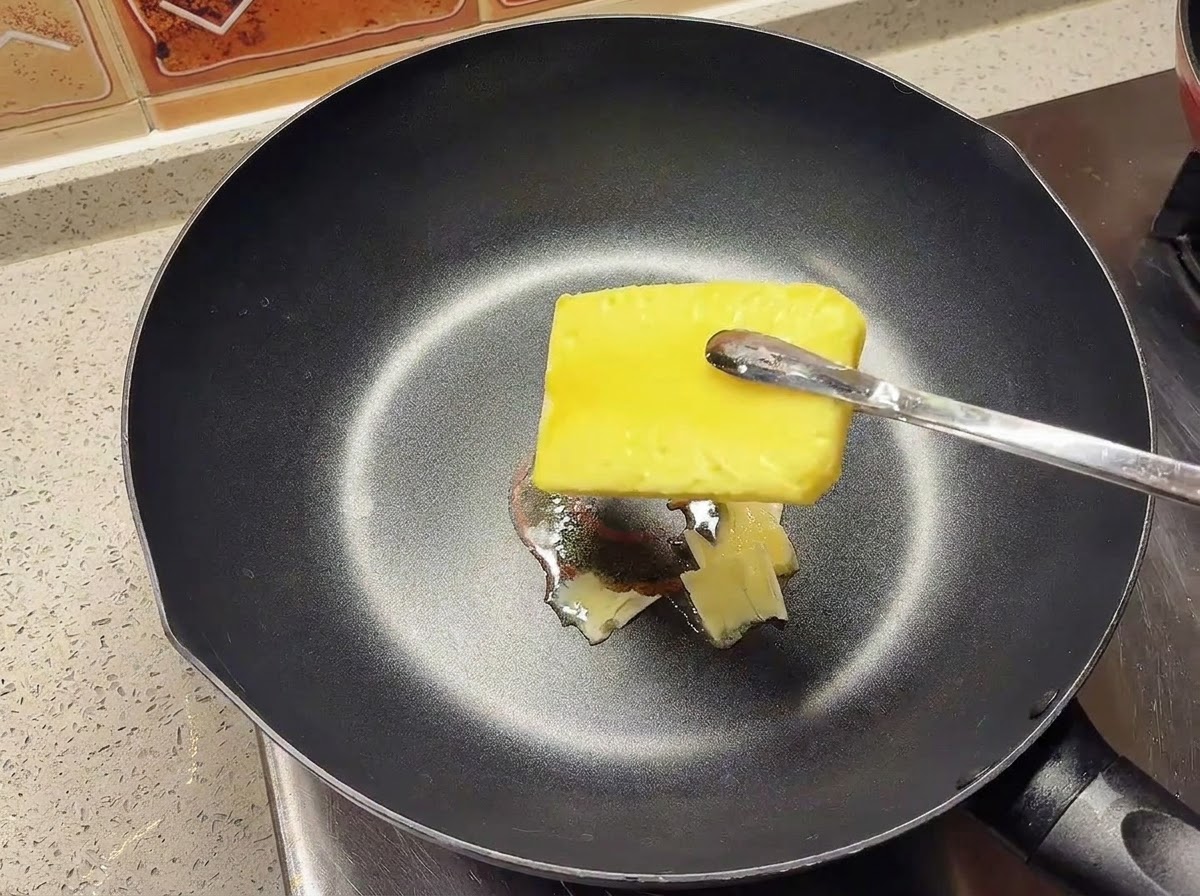 A block of yellow butter melting in a hot black skillet.