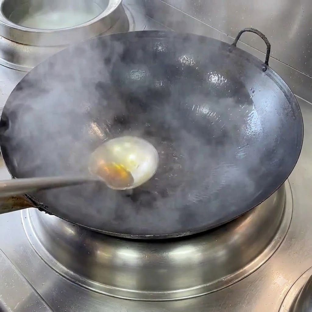 A smoking cast iron wok with a ladle and hot oil being heated on a stove.