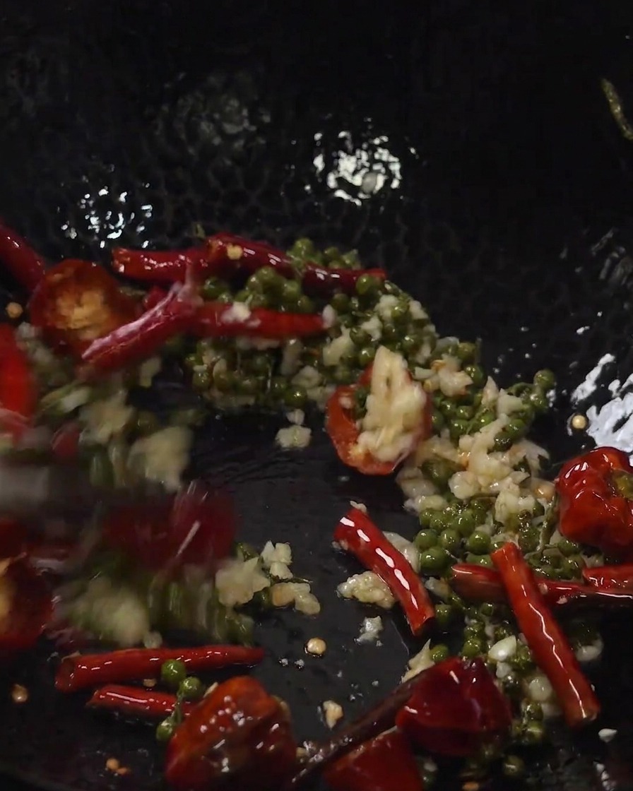 Fried pork ribs and aromatics being tossed together inside a wok.