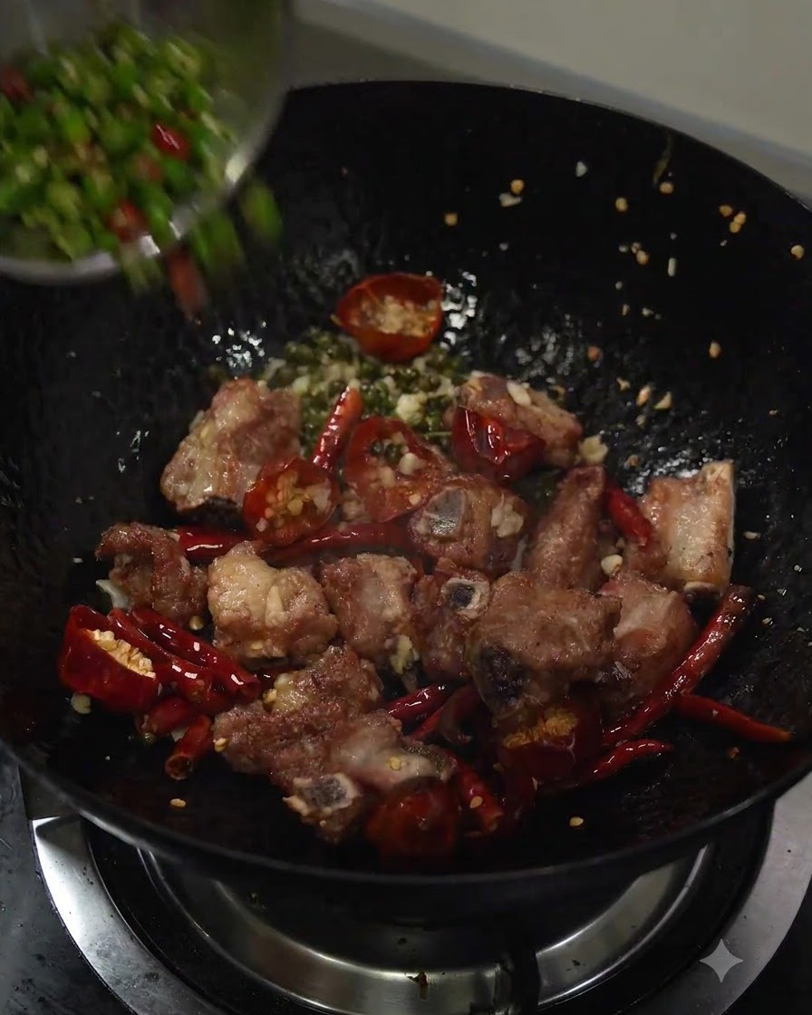 Sliced green chili peppers being poured into the wok with the stir-fried pork ribs and aromatics.