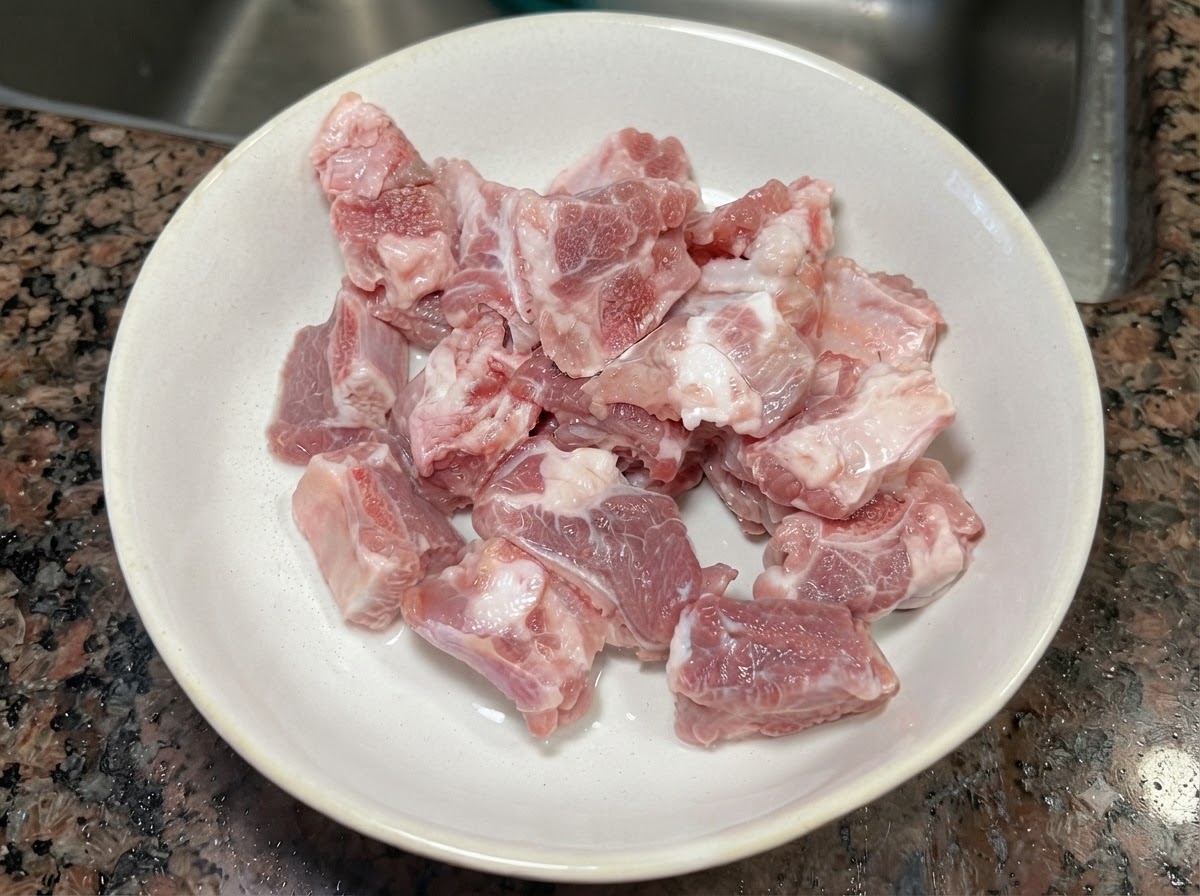 Fresh raw pork rib pieces resting inside a white ceramic bowl.