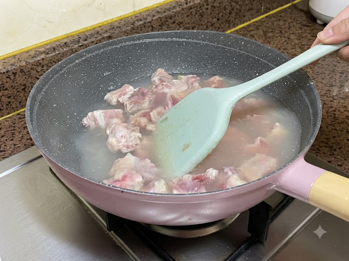 Pork ribs boiling in water inside a pan while being stirred with a light blue silicone spatula.