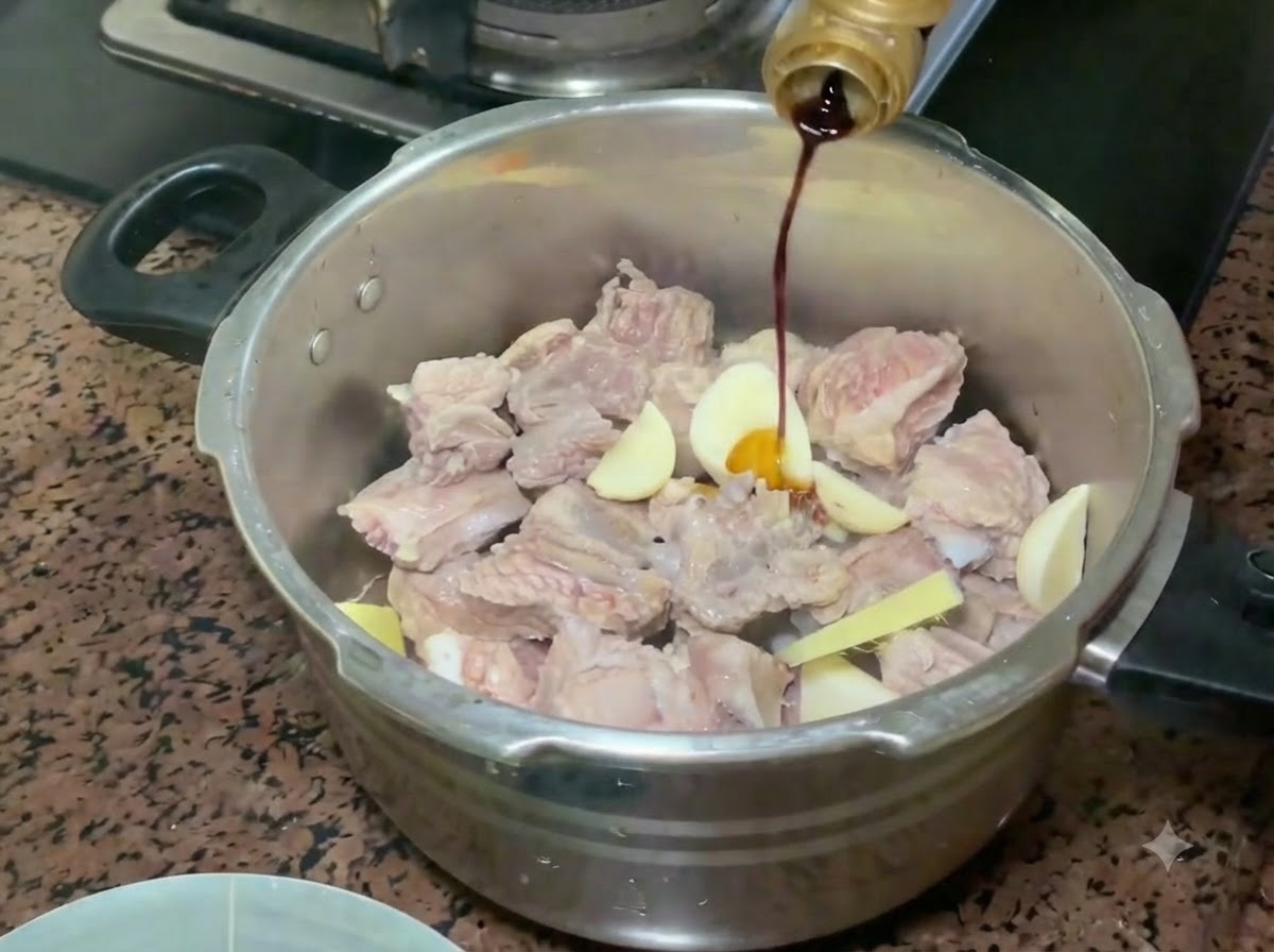 Light soy sauce being poured from a bottle onto the pork ribs and aromatics in the pressure cooker.