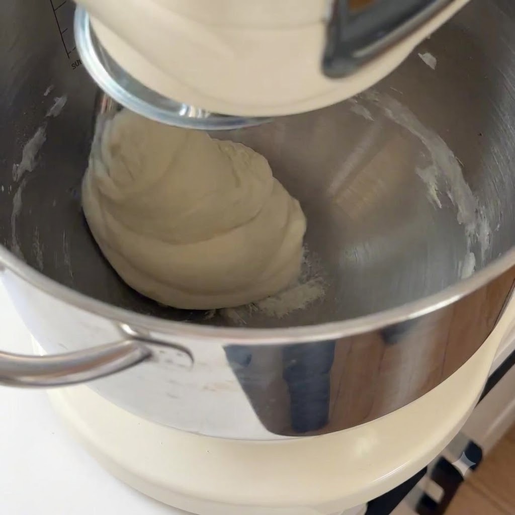 Smooth pizza dough being kneaded inside a large stand mixer bowl.