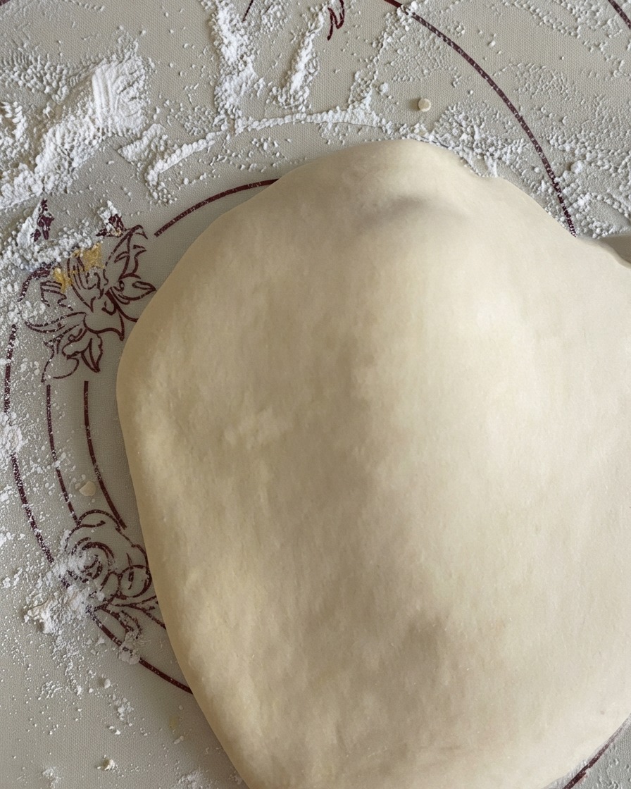 Stretched round pizza dough resting on a floured silicone mat.