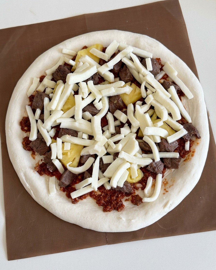 Shredded white mozzarella cheese generously scattered over the meat and pineapple pizza toppings.