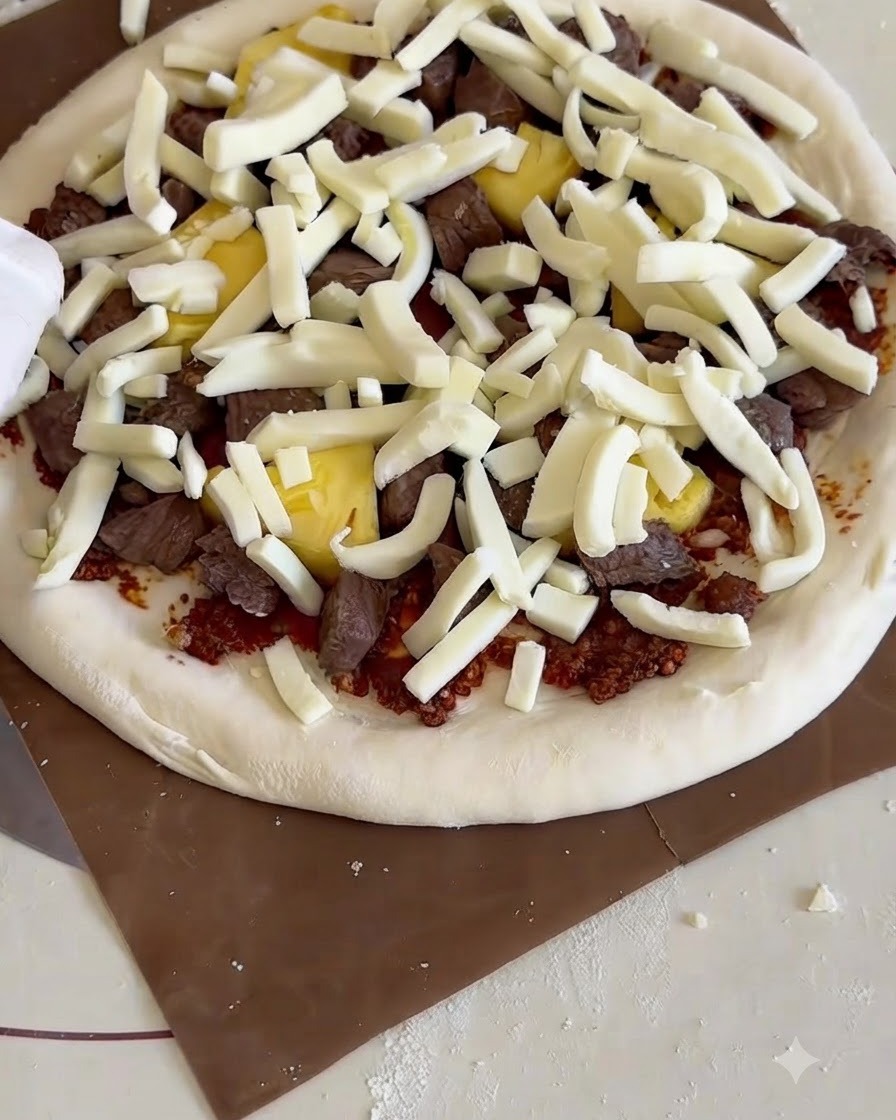 A raw assembled pizza on a wooden peel being slid into a countertop pizza oven with a baking stone.