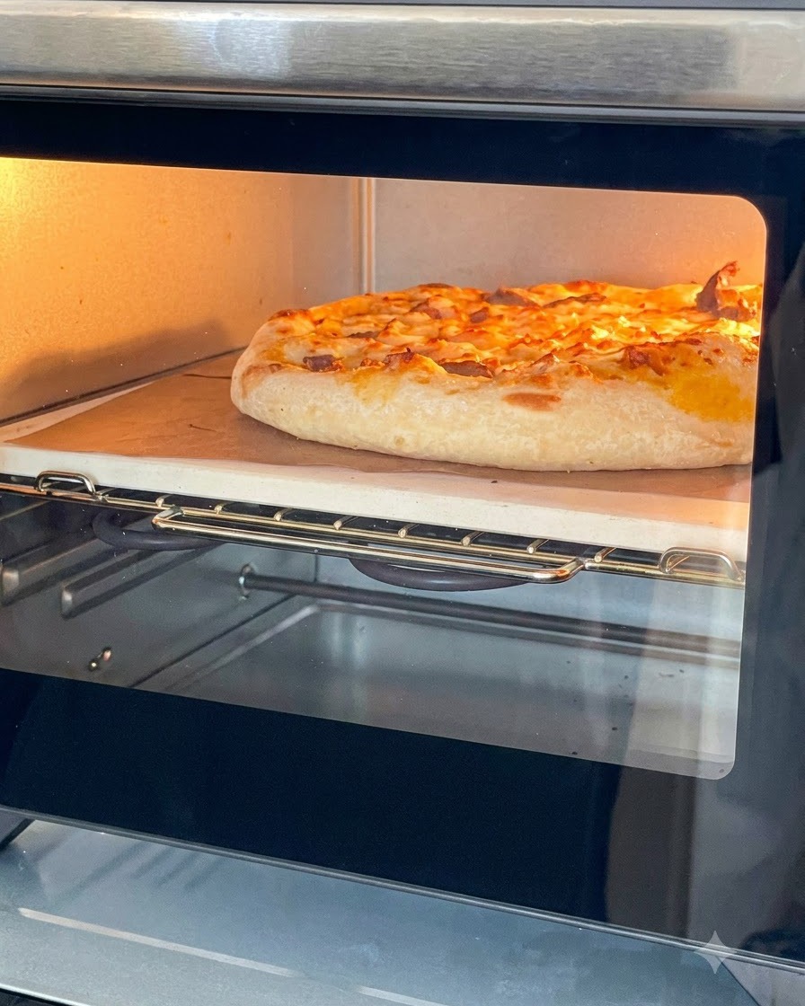A golden, baked pizza with melted cheese inside a small countertop oven on a baking stone.