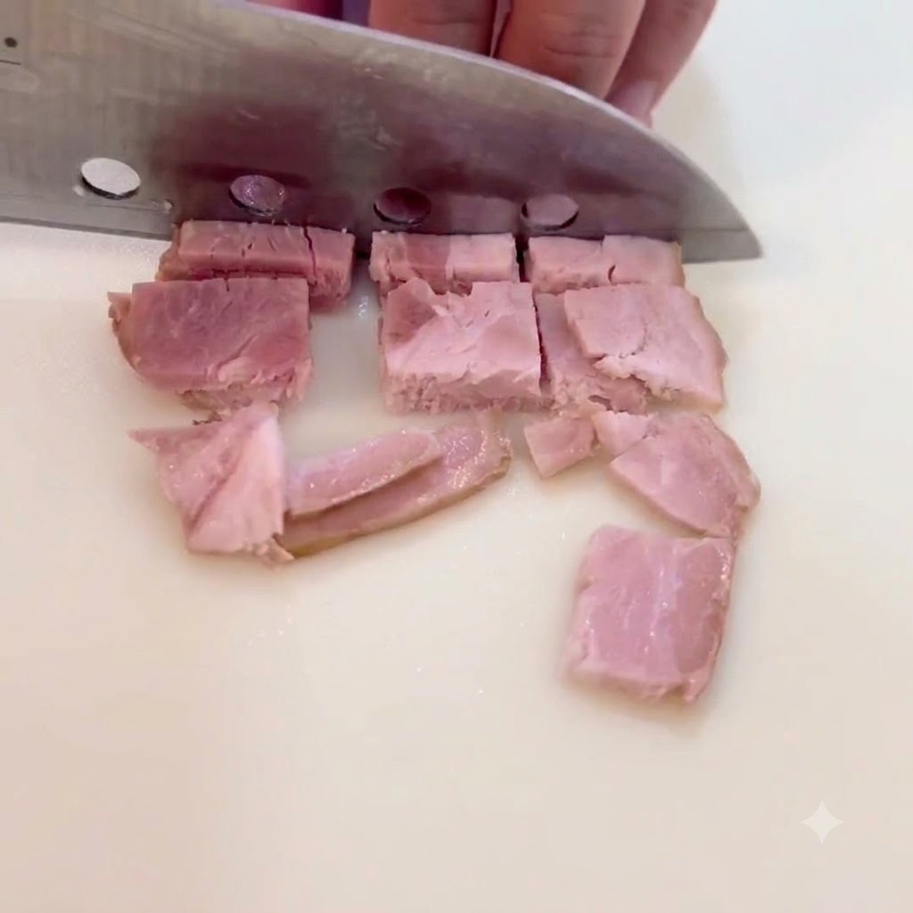 Bacon slices being chopped into small square pieces on a cutting surface.